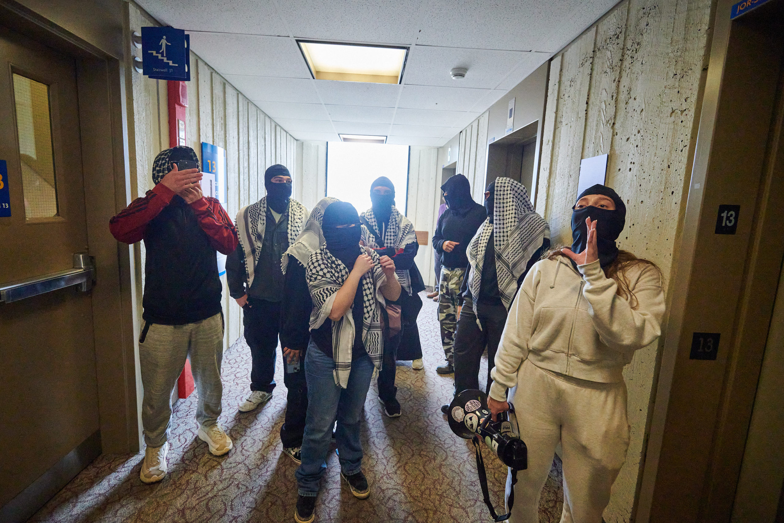 demonstrators articulate demands through megaphone at glass door flanked by two security guards