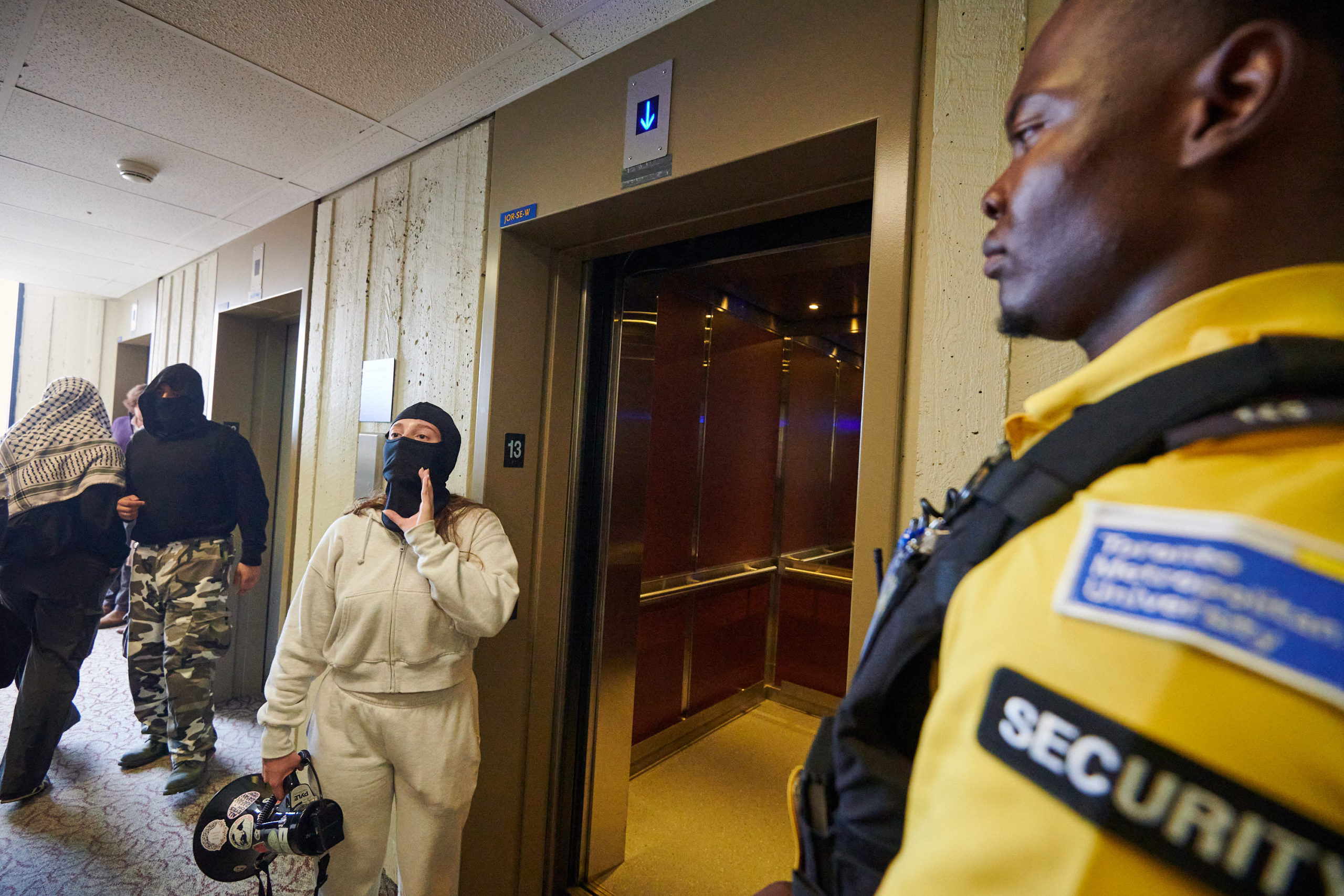 demonstrators articulate demands through megaphone at glass door flanked by two security guards