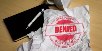 A red stamp reading "DENIED" sits a crumpled piece of paper on a wooden desk.