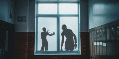 A window of Kerr Hall is lit up by a mysterious light, with the silhouettes of two zombies approaching it