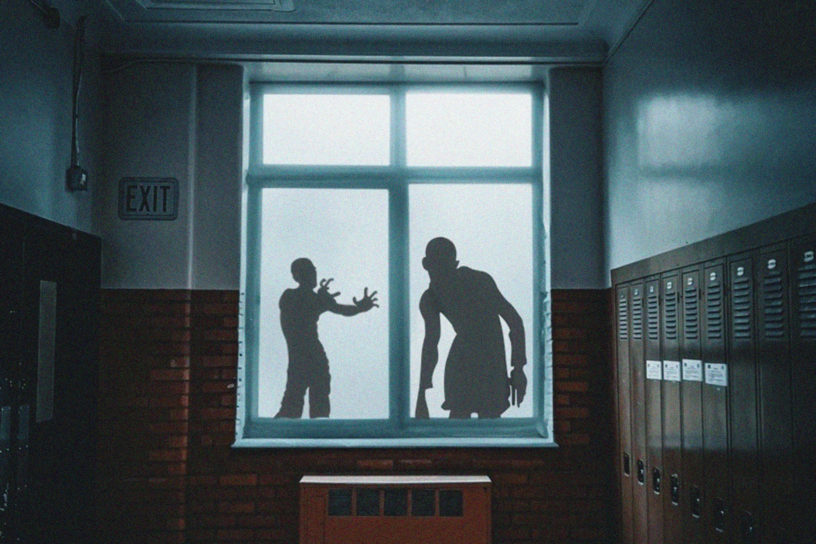 A window of Kerr Hall is lit up by a mysterious light, with the silhouettes of two zombies approaching it