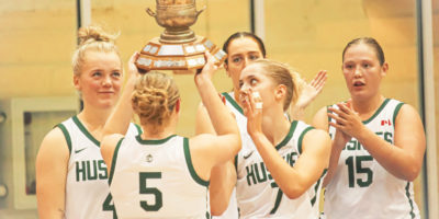 Saskatchewan Huskies guard Gage Grassick lifts the Darcel Wright Memorial Classic trophy over her head with her teammates