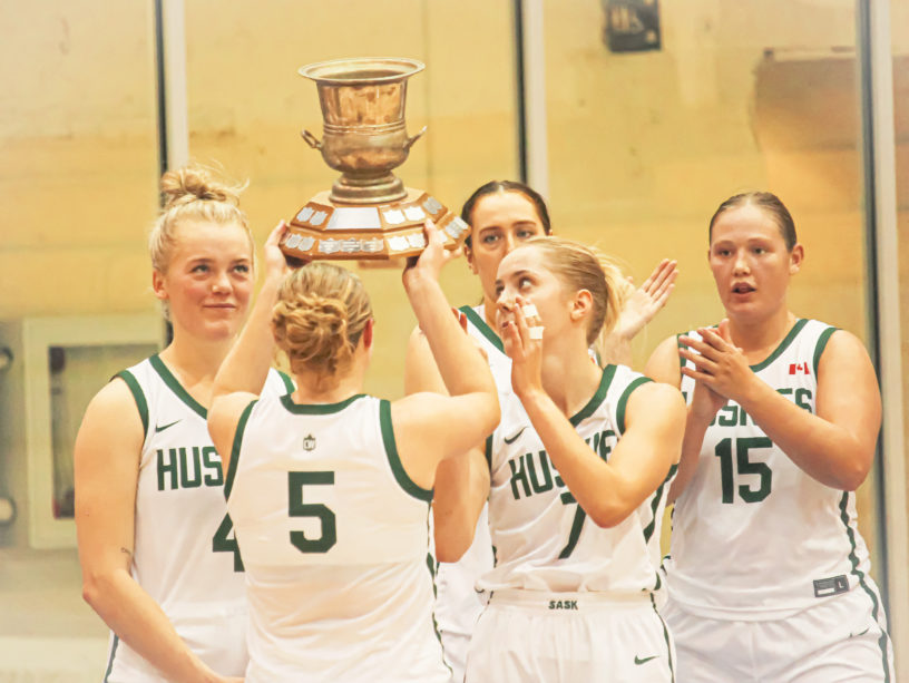 Saskatchewan Huskies guard Gage Grassick lifts the Darcel Wright Memorial Classic trophy over her head with her teammates