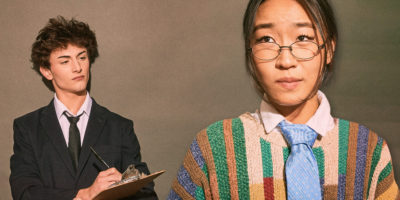 A photo composite of a man in a suite taking notes on a clipboard, staring at a nervous employee