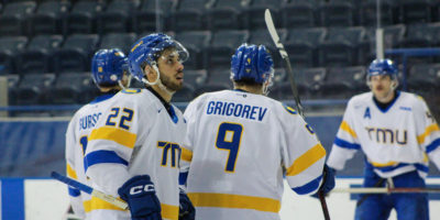 Players on the TMU Bold men's hockey team gather and look up at the scoreboard