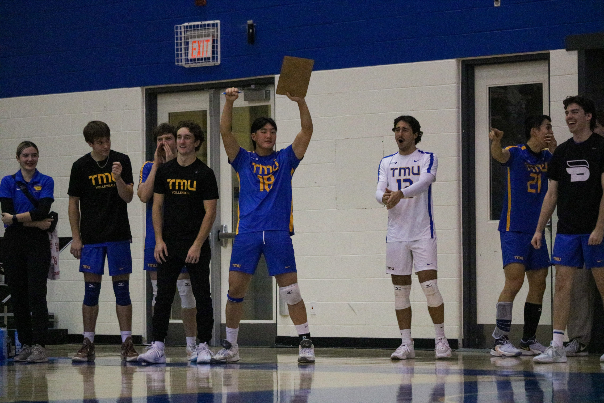 Evan Moua celebrates with a clipboard in his hand while other players on the bench exclaim after a point