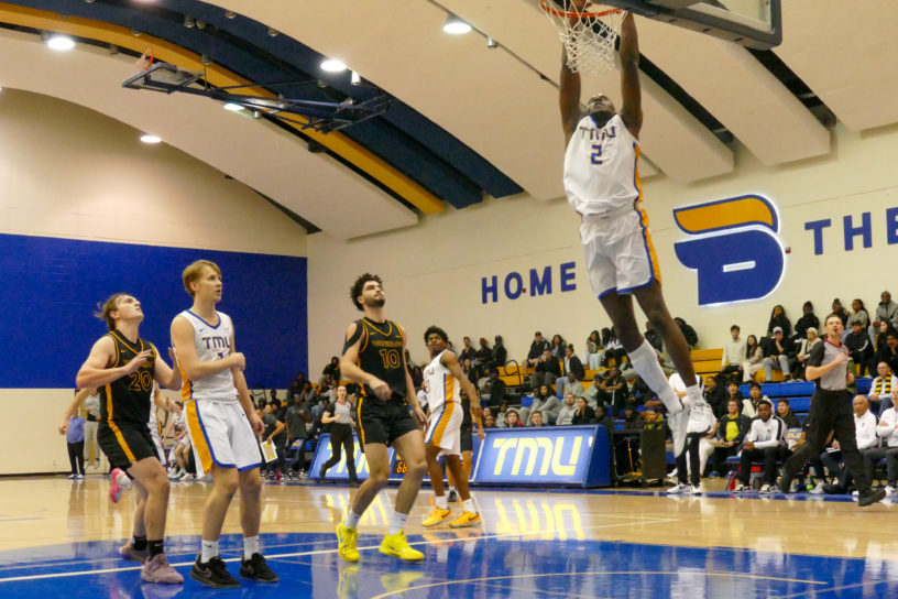 Galand Okeugo dunks a basketball as TMU and Waterloo players watch