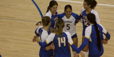 TMU women's volleyball players huddle in celebration after a point