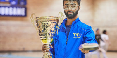 Ahsan Sajjad, member of the TMU cricket team holding the trophy for national champions and pointing the camera with a bat