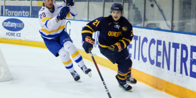 Evan Brand chases a Queen's player behind the net