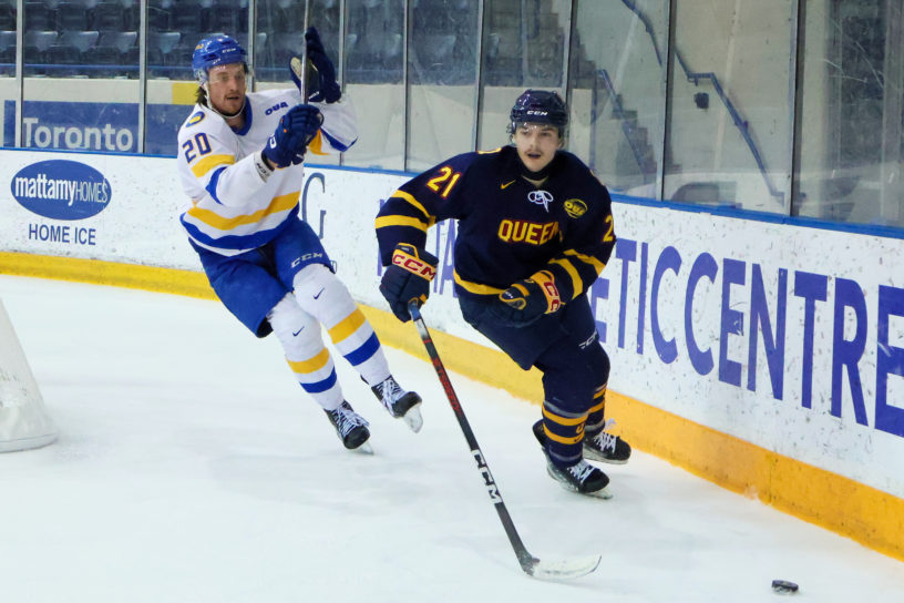 Evan Brand chases a Queen's player behind the net