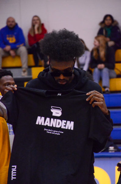 Chris Boucher holds up and looks at a TMU Bold basketball "mandem" shirt