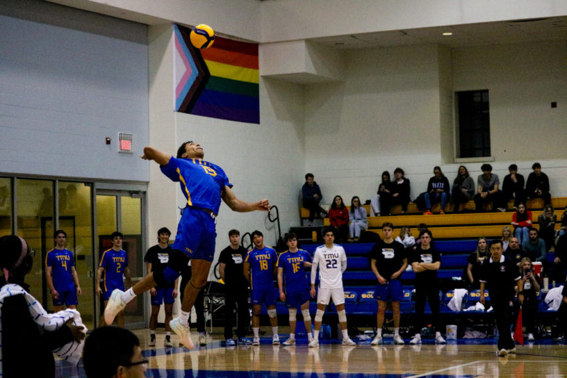 Jacob Walker serves a ball from the air as his team watches from the bench