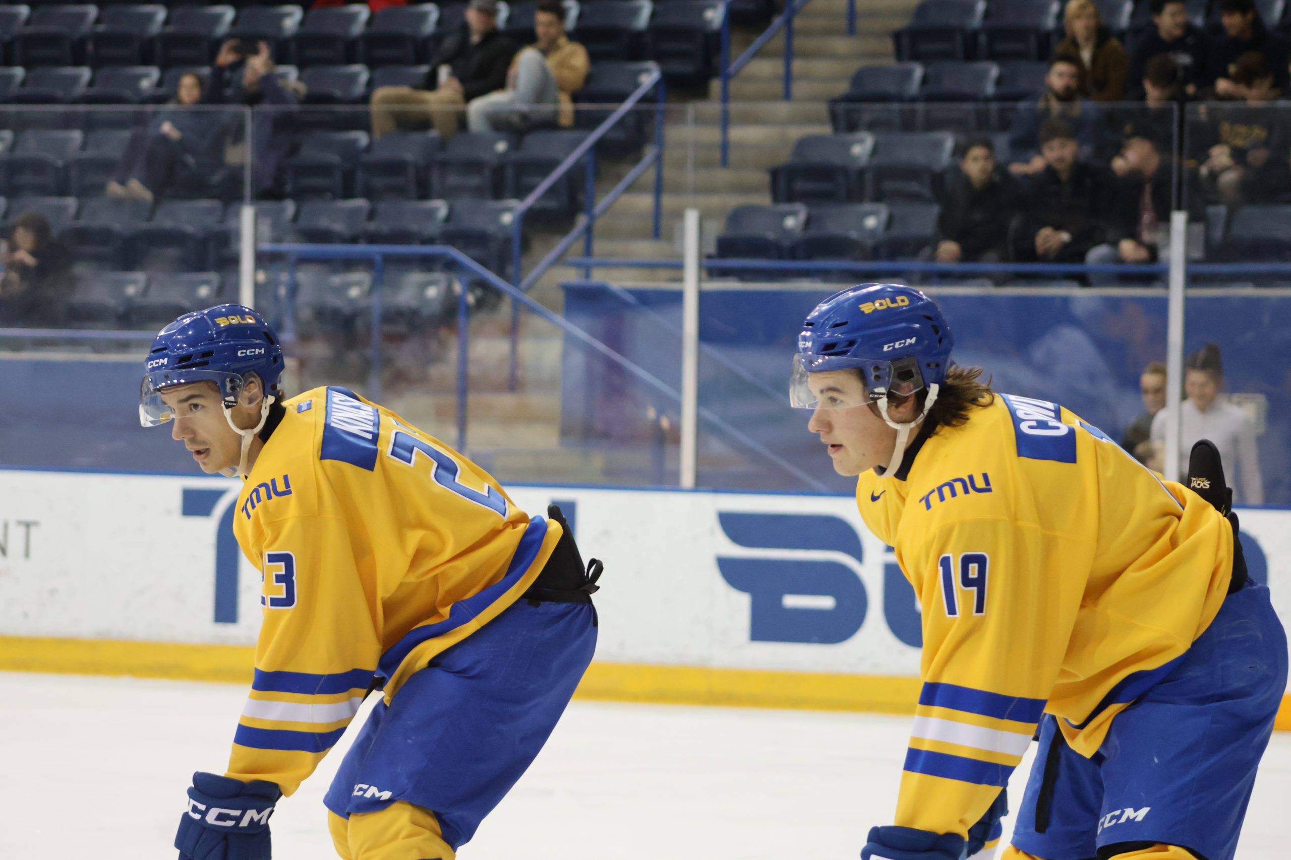 Jaden Condotta and Matthew Kinash prepare for a faceoff in gold TMU Bold jerseys