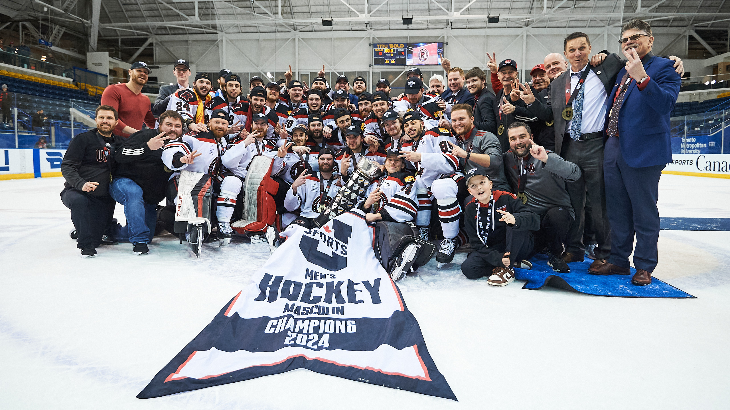 The UNB Reds take a photo with the U Sports men's hockey championship banner and trophy