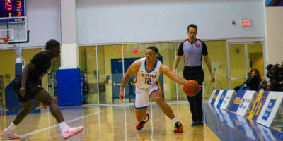 Aaron Rhooms dribbles the basketball in his left hand as he stretches around a McMaster player