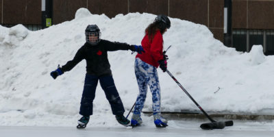 Akira and Apollo Murphy play with hockey sticks and a puck near the edge of the rink on Lake Devo