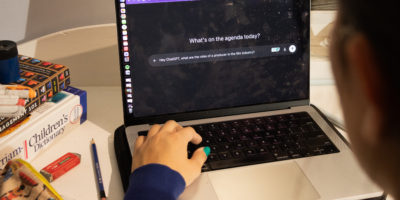 An over-the-shoulder shot of an individuals computer screen with ChatGPT open. There are books and stationary in the background on the left.