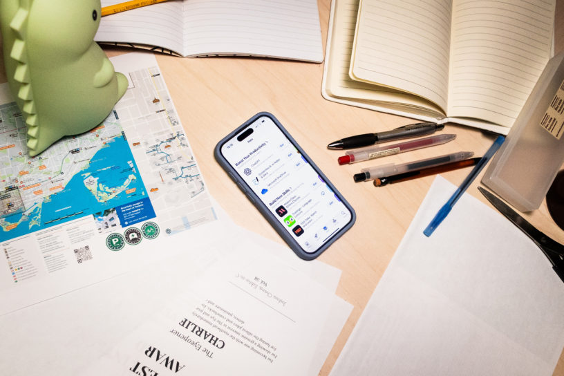 A phone in the middle of a desk with the Apple app store open and loose papers, notebooks and stationary around it.