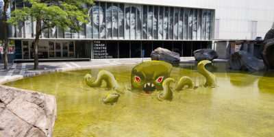 An illustration of a swamp monster emerging from a green coloured Lake Devo.