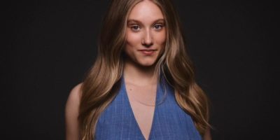 Photo of Paloma Stweart on a black background, wearing a blue top.