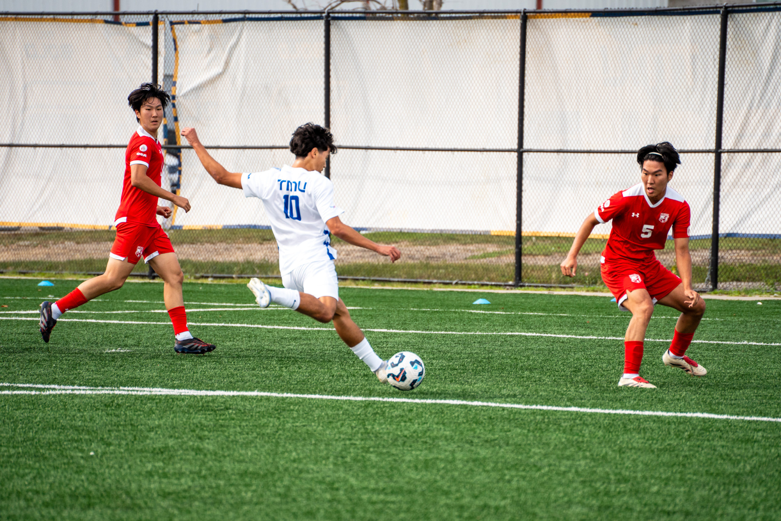 A TMU soccer player kicks the ball amidst his RMC opponents