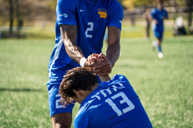 A TMU soccer player helps his teammate up from the ground