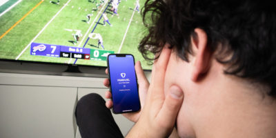 Stressed person sitting in front of a TV with their phone in their hand, with the fan duel app open.