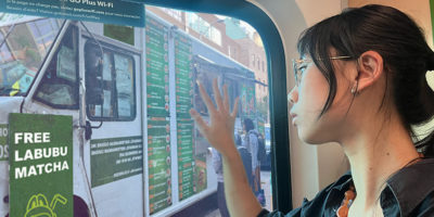 Picture of student looking sadly out a window with her hand on the window. Outside the window is a food truck with a big sign that says “FREE LABUBU MATCHA.”