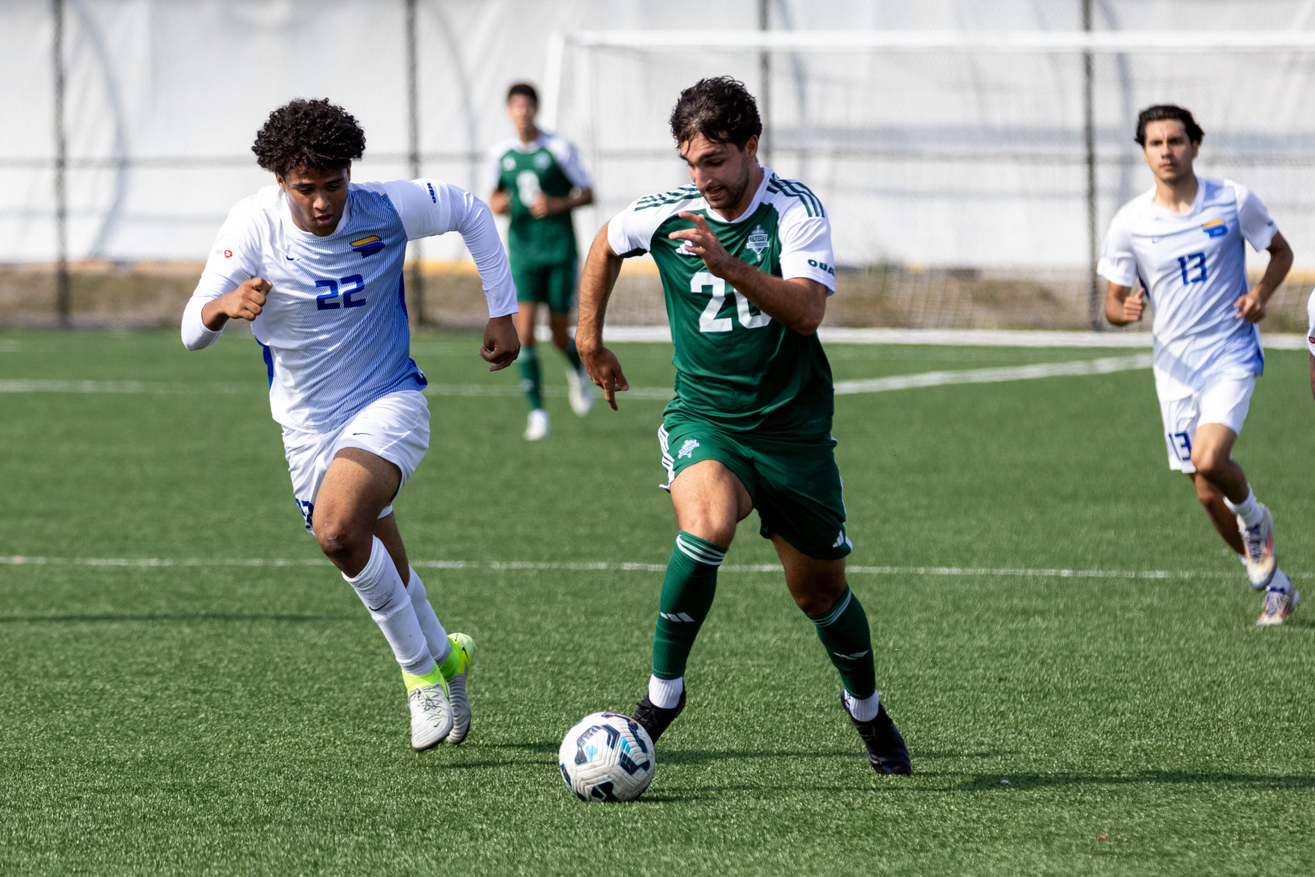 A Trent player with the ball and Manvir Athwal running side by side down the pitch