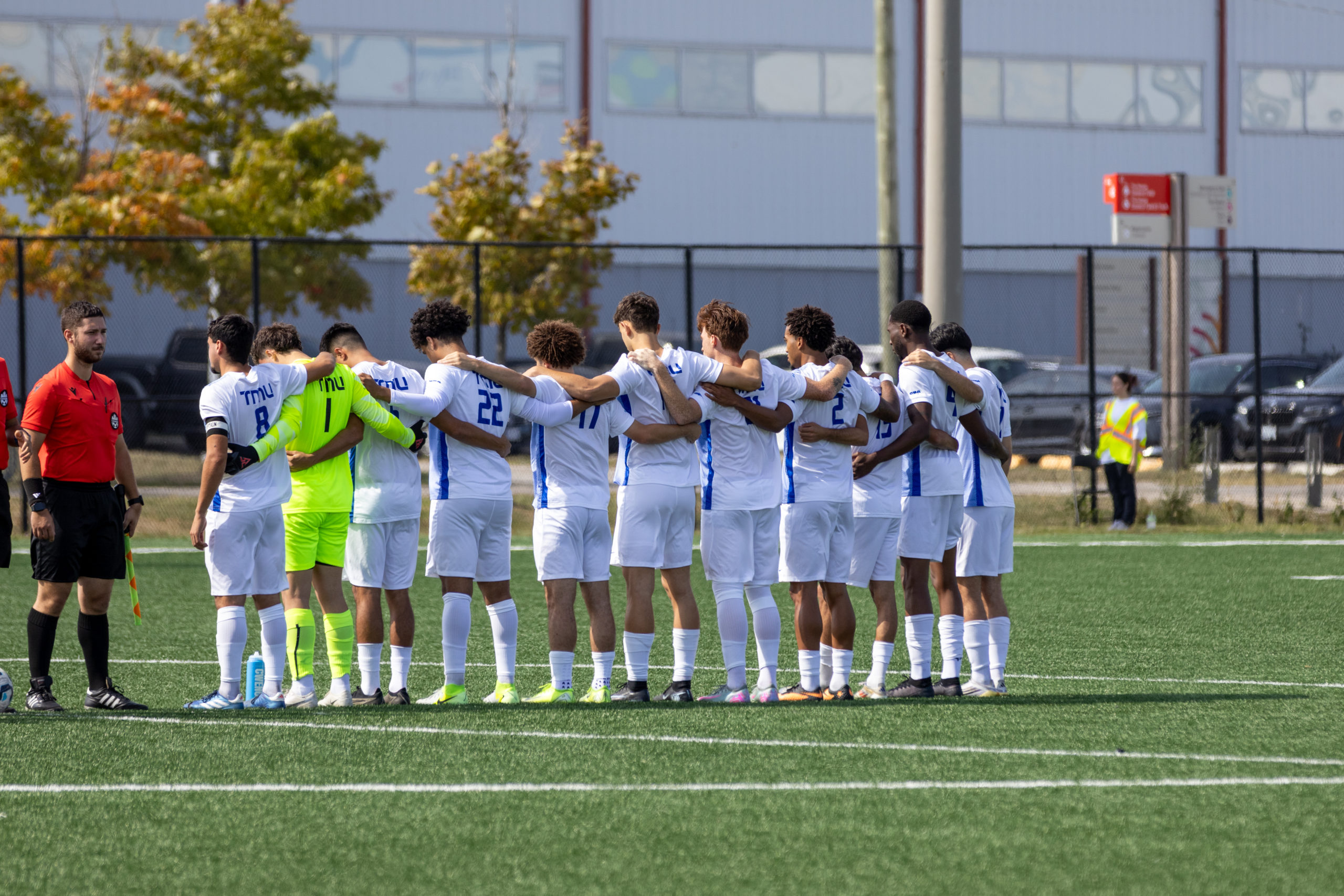 TMU Bold team lining up in between half and the top of the penalty box to watch Trent take a penalty kick