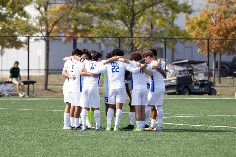 TMU Bold men's soccer huddle together in the middle of the pitch at Downsview Park