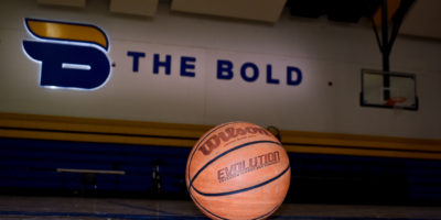 A basketball sitting on the floor of the gym with the Bold logo on the wall in the background.