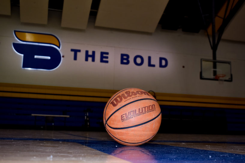 A basketball sitting on the floor of the gym with the Bold logo on the wall in the background.