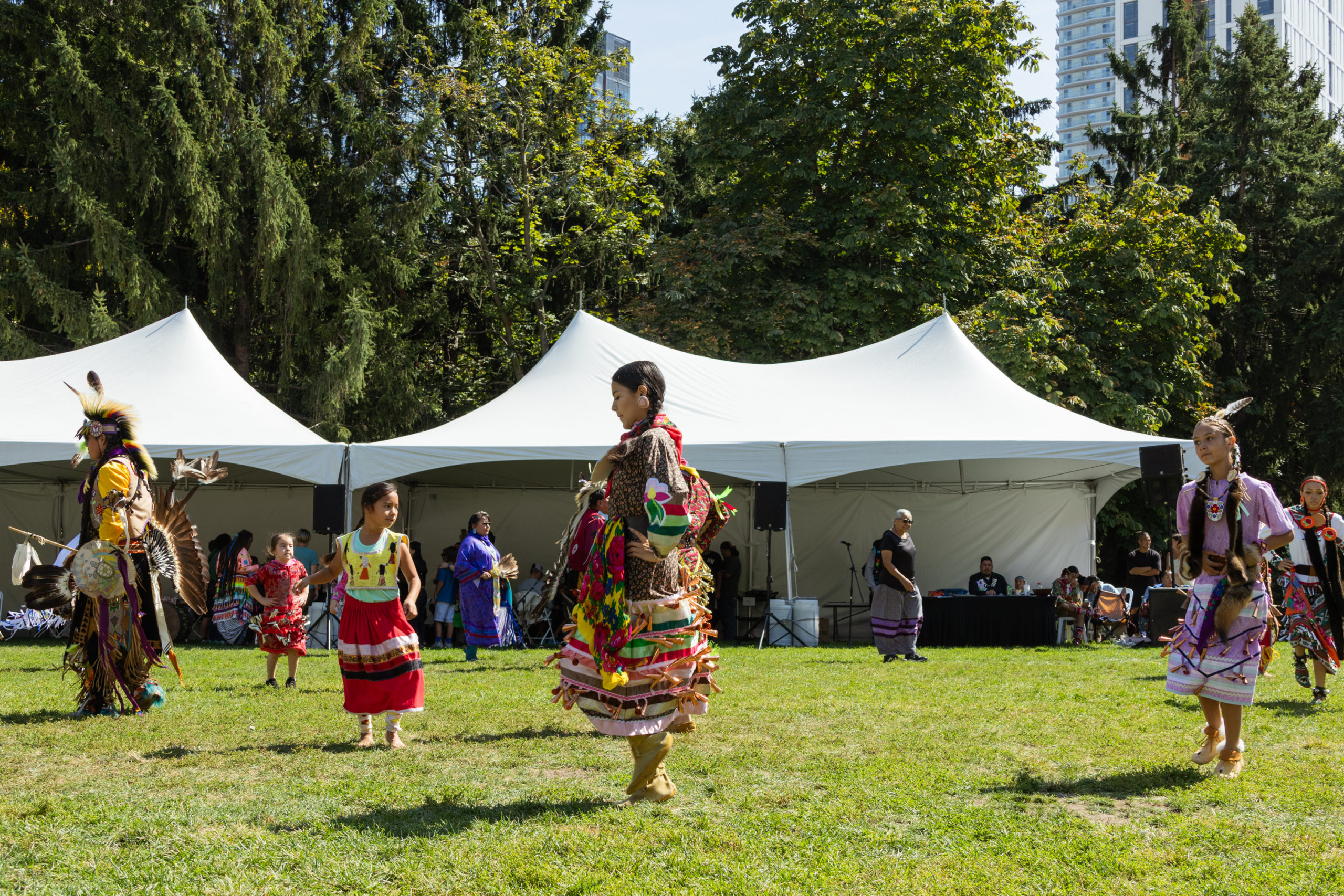 Six dances spaced out on the middle of a field dancing in traditional regalia.