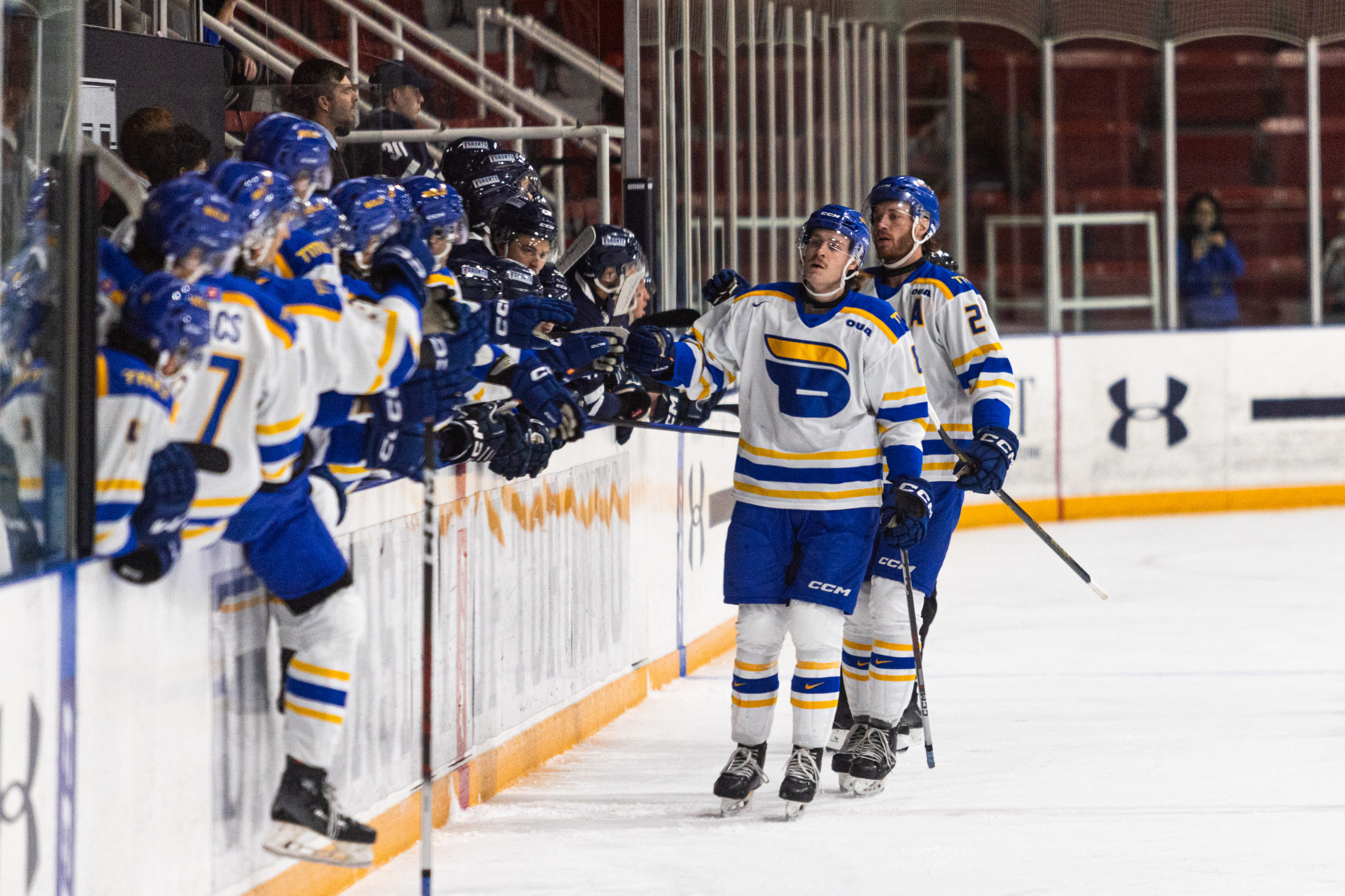Two TMU players skating past the TMU bench to give each player a fist bump