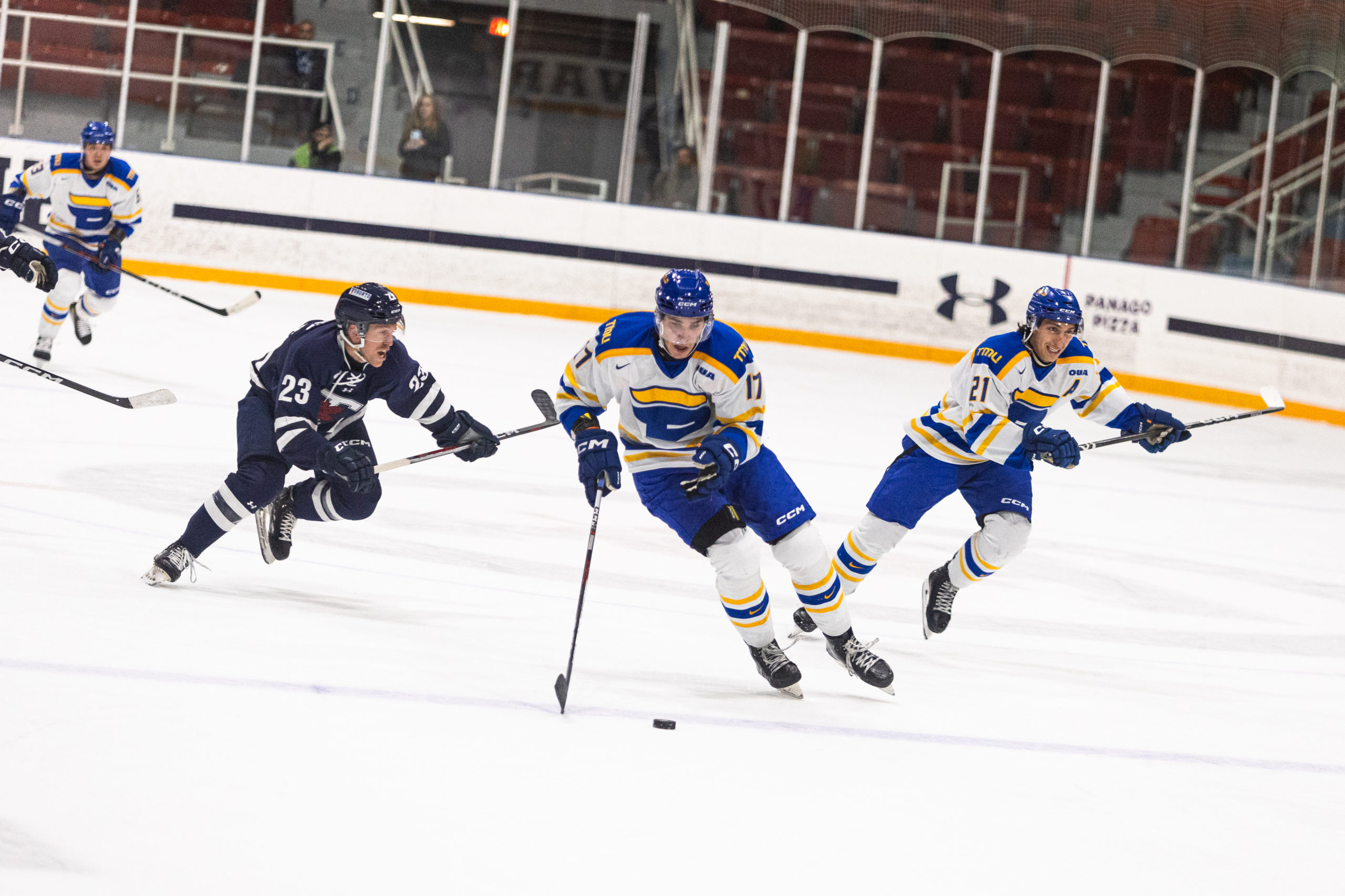 Two TMU players and one U of T player on the left race after the puck that is in TMU's possession