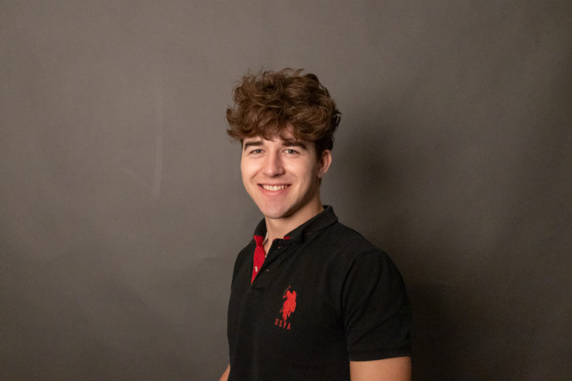 Image of a person on a dark grey background wearing a black shirt with a red logo.