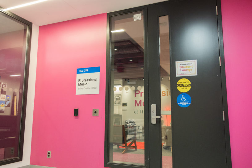 Image of the outside of a room with a pink wall with a sign titled "professional music student lounge"