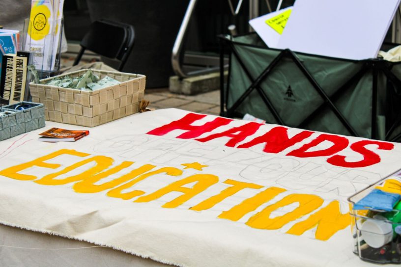 Image of a banner on a table that reads "hands of our education"