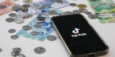 A phone sits on a desk with the TikTok app open, surrounded by bills and coins.