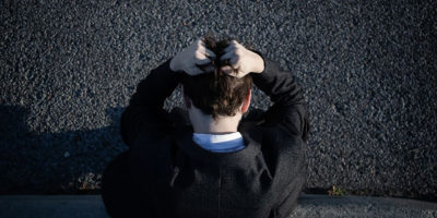 A birds eye view image of a person in a suit on the side of the sidewalk with their fists in their hair.