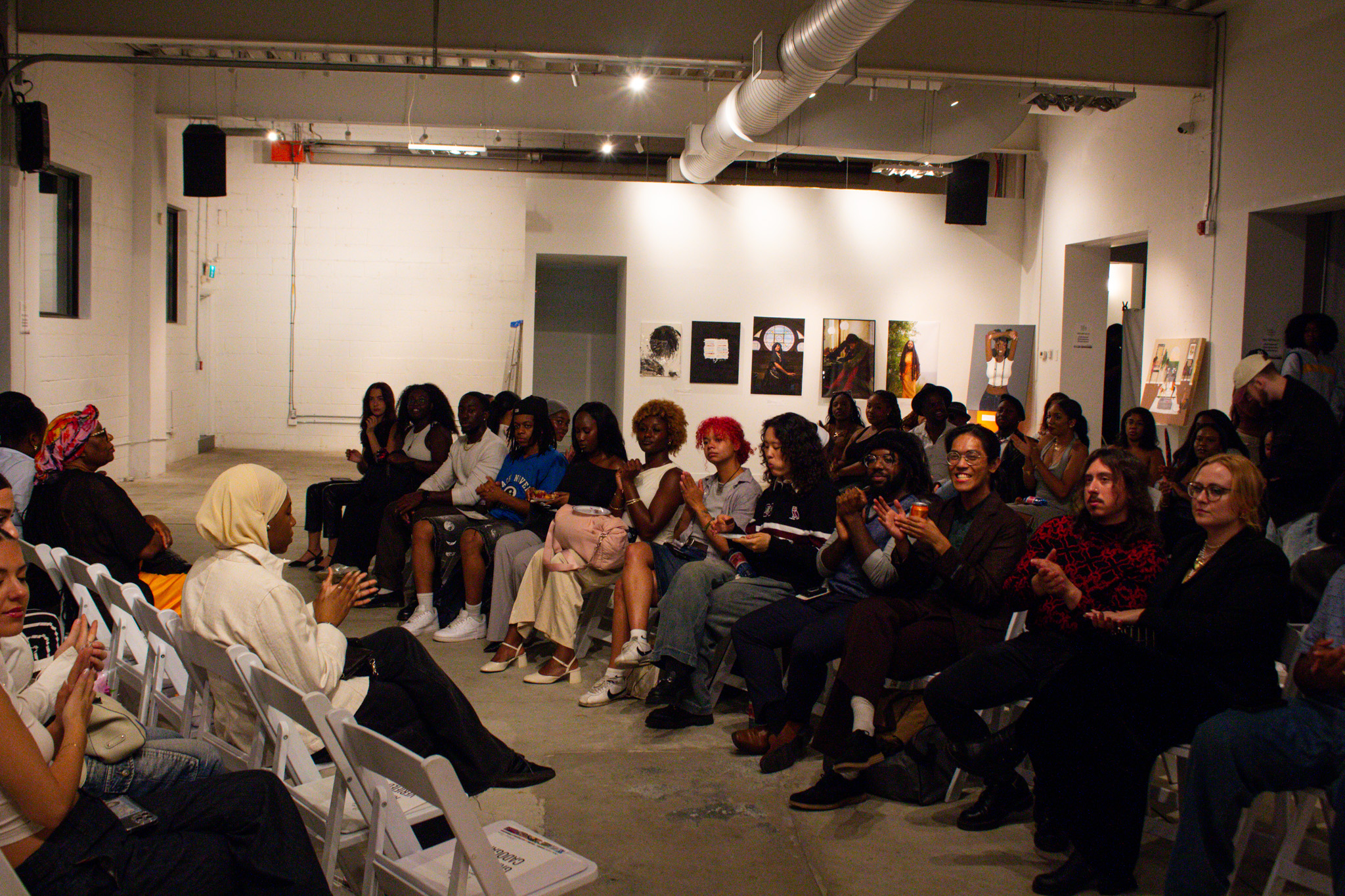 A group of people sitting on white chairs lined in rows.