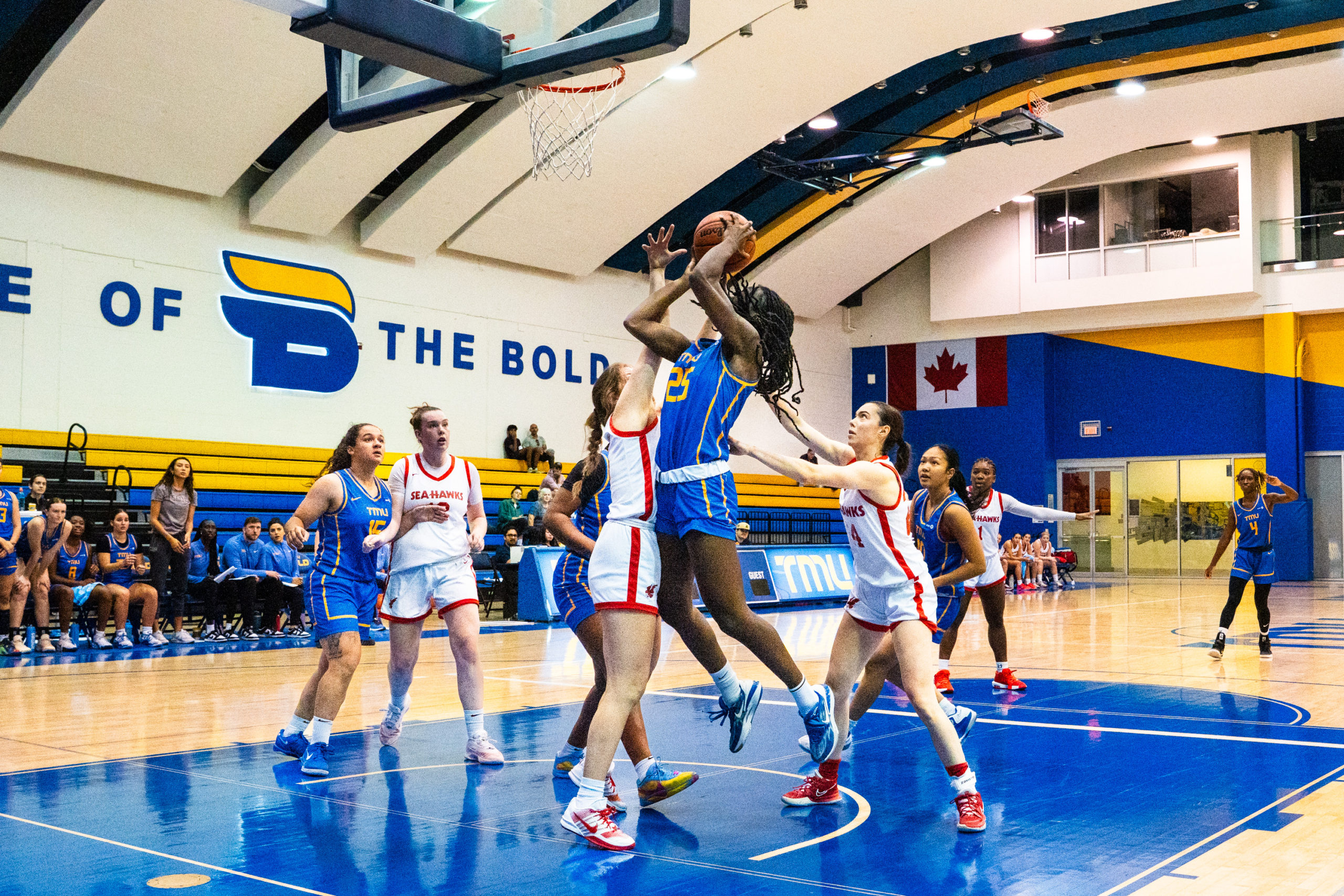 A TMU basketball player attempts a basket as opponents reach towards her