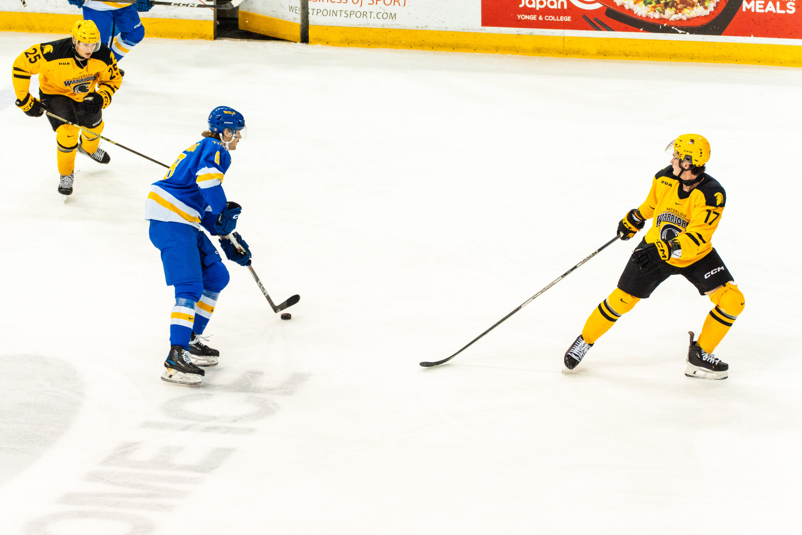 Two Waterloo players surround a TMU player with the puck