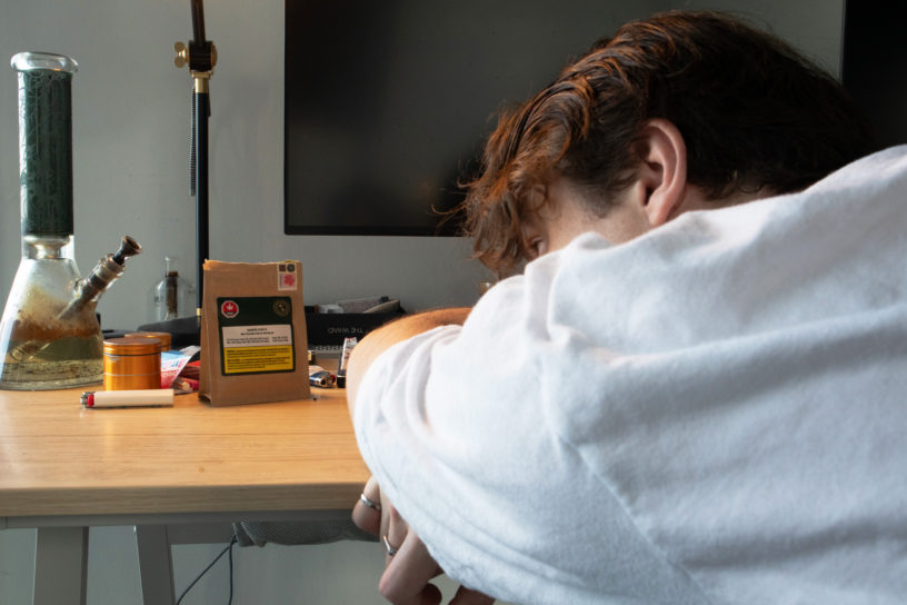 A person is laying their head on a desk looking at a package of THC and various other objects.