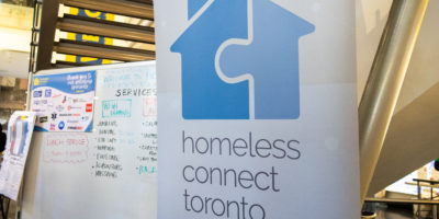 Image of a banner with a blue logo in the shape of a house and that reads "homeless connect toronto."