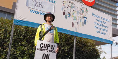 Image of a person holding a sign in front of a Canada Post building.