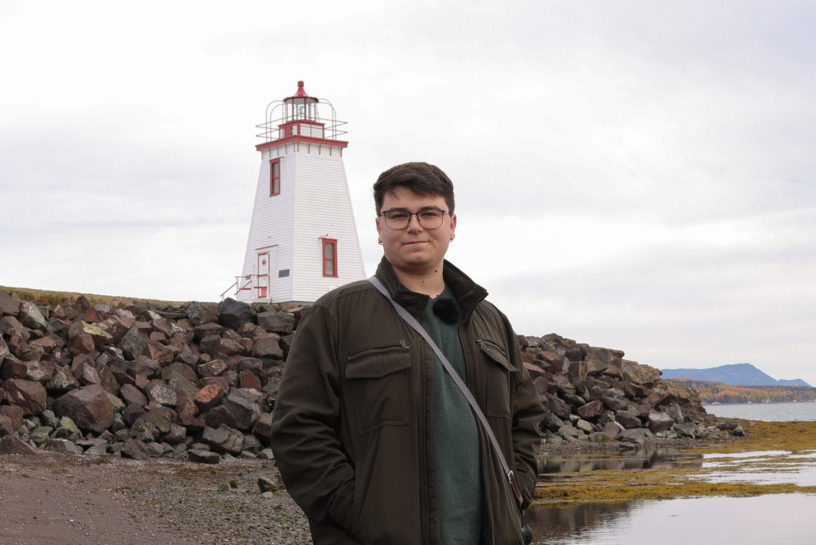 Image of Daniel Opasinis looking at the camera with a lighthouse in the background.