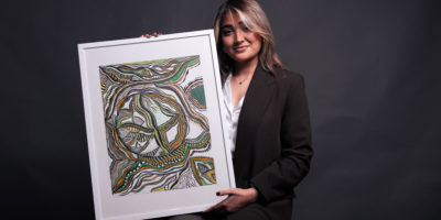 Woman looking upwards on a black background while holding a painting.